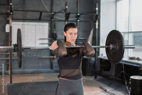 Close up front portriat of a woman is lifting weight while working out with barbell in gym.