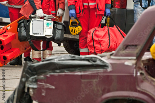 Demonstration of rescue work. Firefighters break into a car after an accident. Rescue team retrieve the victim from the burned car. Doctors in the background are preparing to provide first aid.