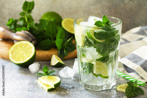 Summer cold drink and cocktail. Fresh Mojito cocktail with lime, ice and mint in a glass on a gray stone background.