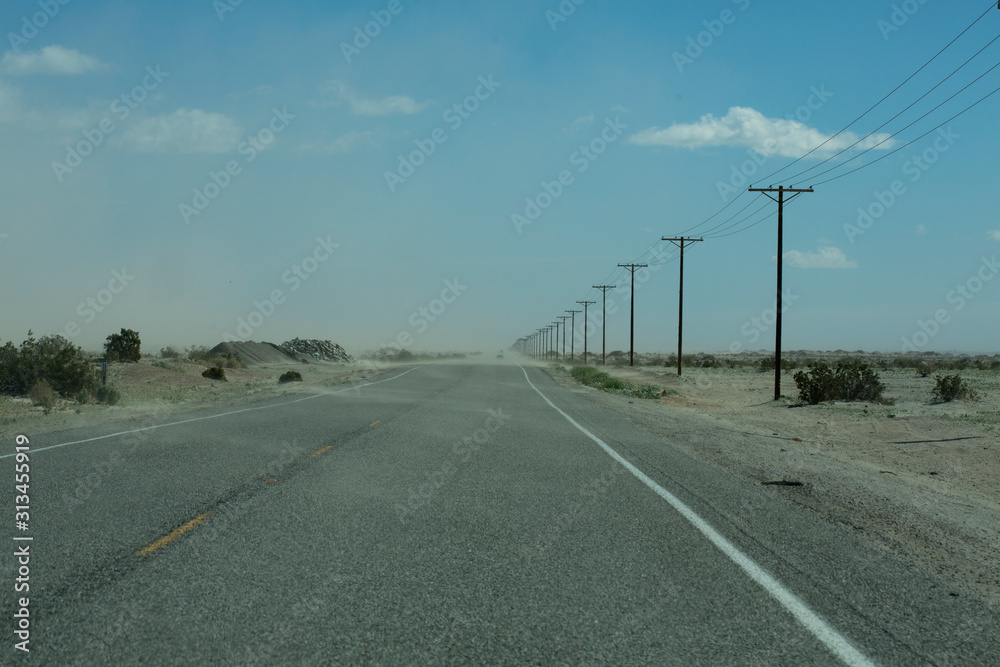 Empty, desolate two-lane highway in desert with blowing sand and power lines