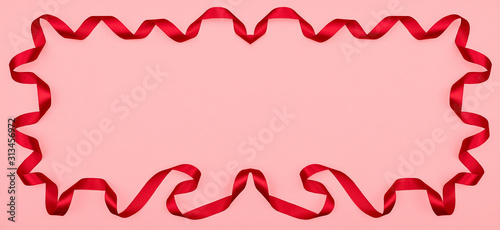 Red wavy ribbon on pink background. Holiday decoration. Valentine's Day decoration congratulation frame.