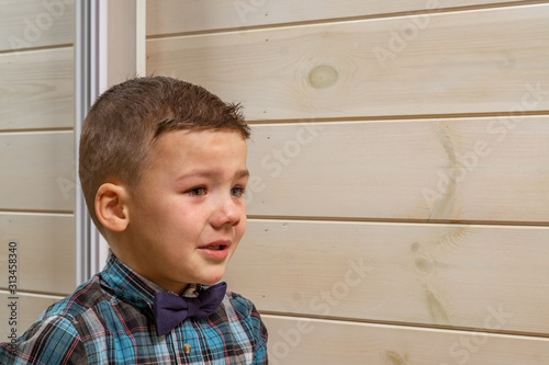 Bild auf Leinwand A 4 years old boy in a blue clerical shirt is crying on a light wooden background