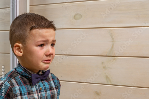 Foto A 4 years old boy in a blue clerical shirt is crying on a light wooden background