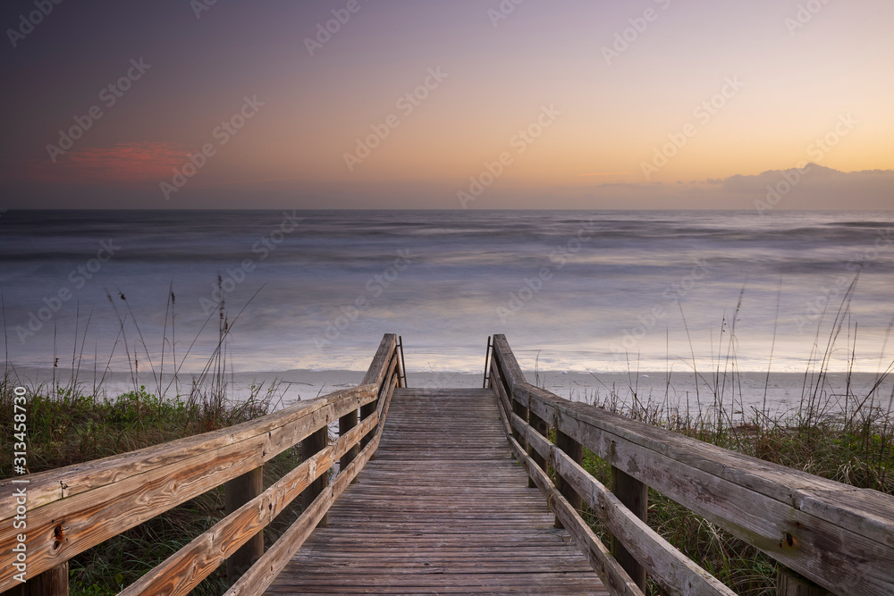 A wood pedestrian bridge, build over a sand dune that is used to give beach access in Daytona Beach, Florida, glows during a morning sunrise.  