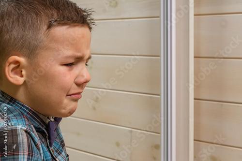 Bild auf Leinwand A 4 years old boy in a blue clerical shirt is crying on a light wooden background