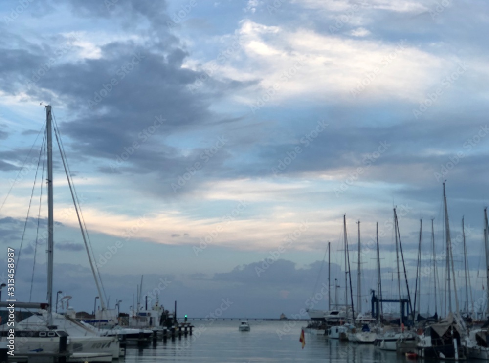 Veleros en el puerto con mastil sin vela al atardecer con cielo nublado