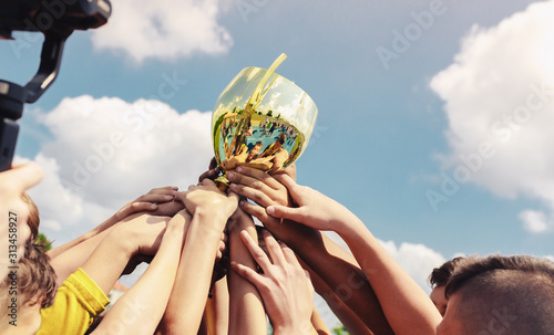 Kids in sports team lift up the golden cup trophy after winning the final tournament match. Children celebrate success in sports. Winning championship in sports.