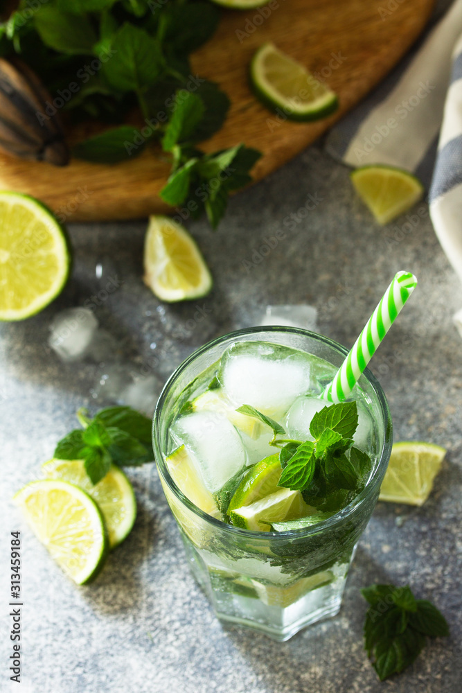 Fresh Mojito cocktail with lime, ice and mint in a glass on a gray stone background. Summer cold drink and cocktail. Fresh Mojito cocktail with lime, ice and mint in a glass on a gray stone background. Summer cold drink and cocktail.