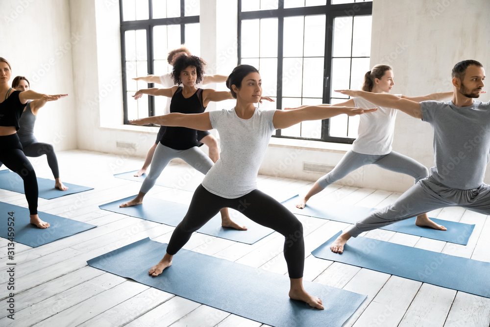 Fototapeta premium Diverse young people doing Virabhadrasan exercise, practicing yoga