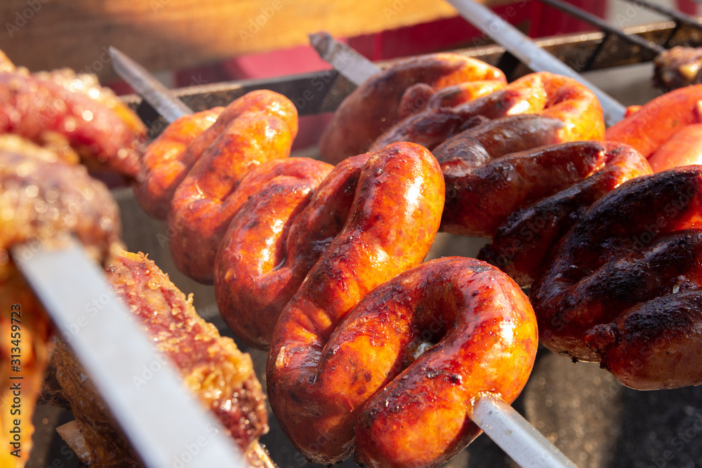 Pieces of skewered sausage being cooked for a barbecue. Bright light and several meats being prepared at the same time. Pieces of skewered sausage being cooked for a barbecue. Bright light and several meats being prepared at the same time.