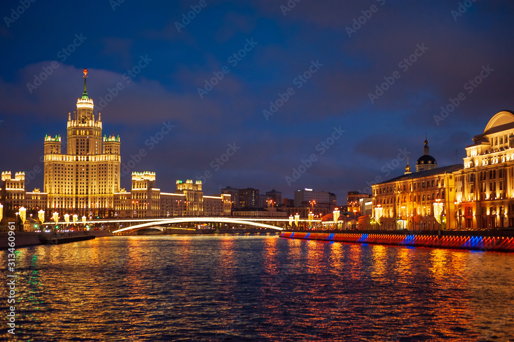 View of illuminated Stalin skyscraper on the festive illumination Kotelnicheskaya embankment and Moscow River at night in Moscow.
