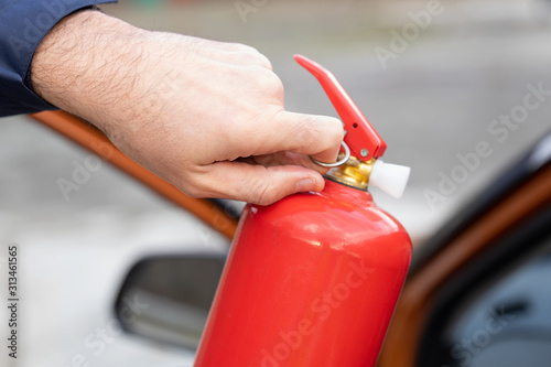 Fotografie Male hand pulling safety pin of fire extinguisher close up against the backgroun