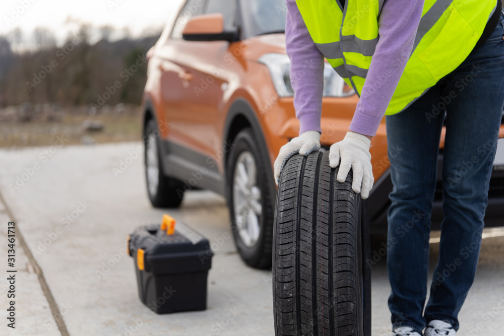 Mechanic holds a tire at the road and rolling tire to repairing service. Transportation and automotive maintenance concept