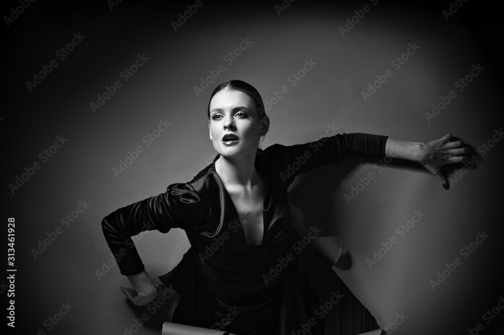 Black and white photo of vogue model posing in little black dress through wrapped paper grey background in studio, dramatic fashion poses, make up and hairstyle Black and white photo of vogue model posing in little black dress through wrapped paper grey background in studio, dramatic fashion poses, make up and hairstyle