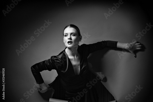 Black and white photo of vogue model posing in little black dress through wrapped paper grey background in studio, dramatic fashion poses, make up and hairstyle