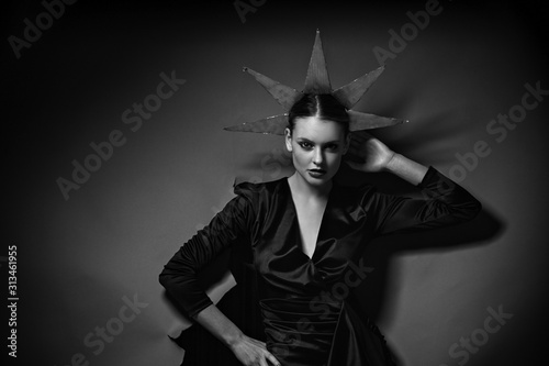 Black and white photo of  vogue model posing in little black dress through wrapped paper grey background in studio, dramatic fashion poses, make up and hairstyle