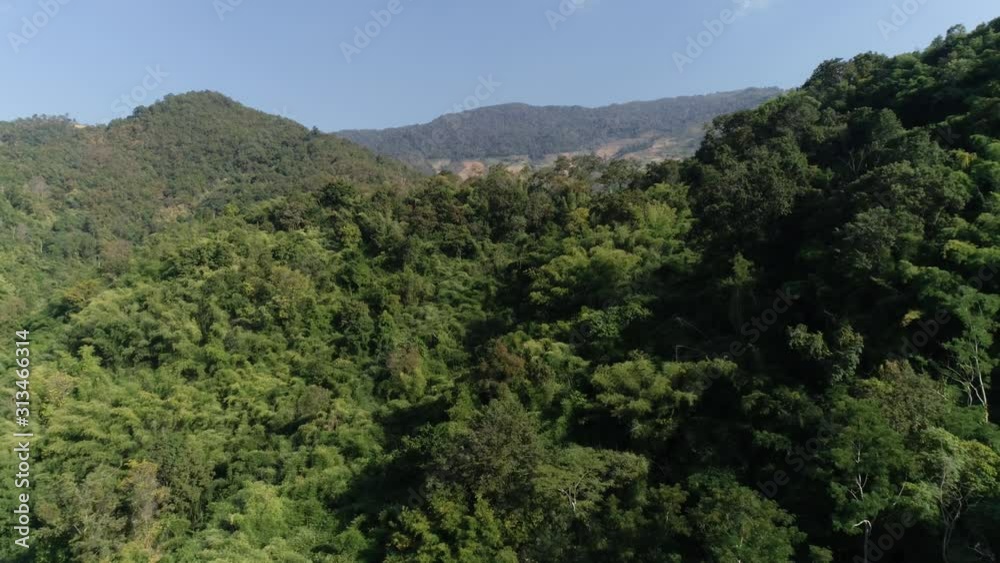 Forward aerial shot towards Southeast Asian mountains with gradual descent and forest below