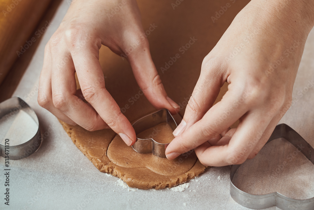 Making gingerbread cookies in the shape of a heart for Valentines Day. Woman hand use cookie cutter. Holiday food concept