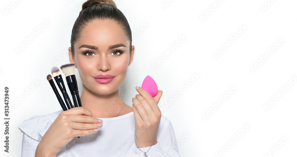 Beauty model girl, makeup artist holding set of make up brushes and sponge. Beautiful brunette young woman with perfect skin and nude make-up closeup. Face contouring. Isolated on white background Beauty model girl, makeup artist holding set of make up brushes and sponge. Beautiful brunette young woman with perfect skin and nude make-up closeup. Face contouring. Isolated on white background