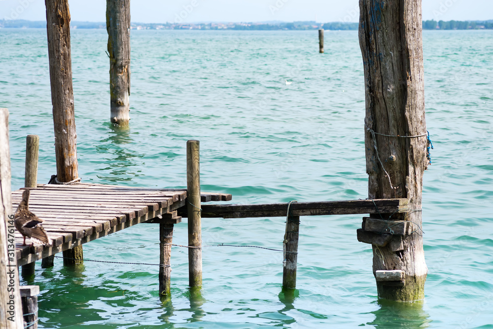 Old bridge with bars with seagulls on landscape of Lake Garda with town Limone sul Garda