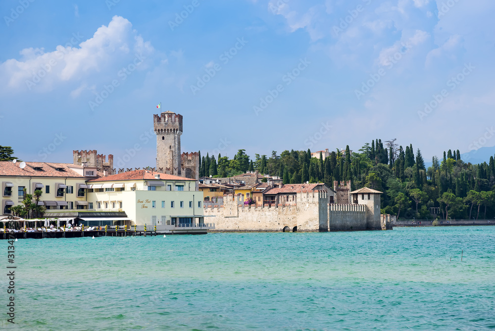 Panoramic view against bright sun rays above the rocks on beautiful Garda lake shore in Riva del Garda city in Lombardy, Italy, surrounded by high dolomite mountains
