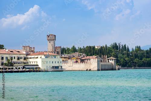 Fototapeta Naklejka Na Ścianę i Meble -  Panoramic view against bright sun rays above the rocks on beautiful Garda lake shore in Riva del Garda city in Lombardy, Italy, surrounded by high dolomite mountains