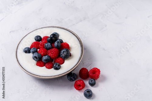 Tasty fresh blueberry raspberries yoghurt shake dessert in ceramic bowl standing on white table background.