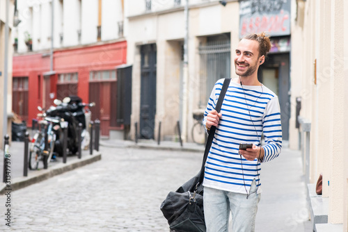 happy young man walking in city listening to music with smart phone and earphones