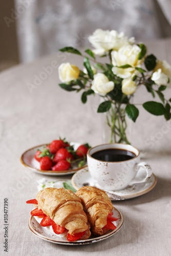 Breakfast in French. Croissant sandwich with I soft cheese and strawberries. And black coffee, a bouquet of flowers. Fresh strawberries. Soft focus. Space for text.  Copy Space