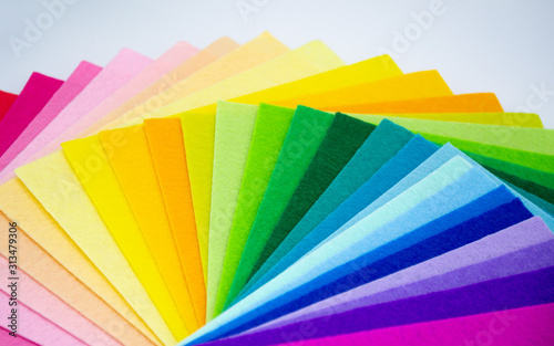 The square pieces of felt spread out by a color spectrum on similarity of a rainbow: from shades of pink, yellow, green, blue, purple and bright violette at the end. White background. Copy space