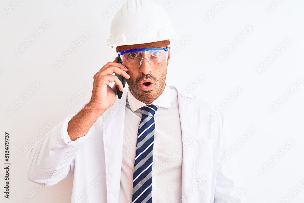 Young scientist man wearing safety helmet and calling using smartphone over isolated background scared in shock with a surprise face, afraid and excited with fear expression Young scientist man wearing safety helmet and calling using smartphone over isolated background scared in shock with a surprise face, afraid and excited with fear expression