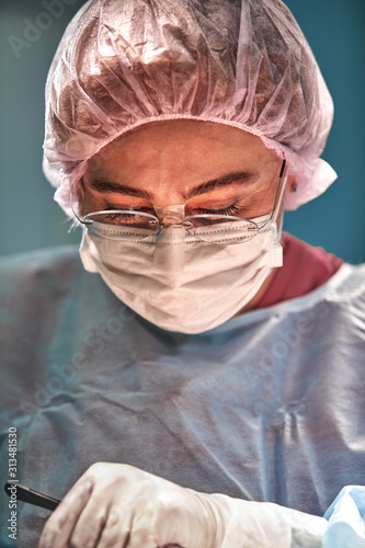 Close up portrait of young female surgeon doctor wearing protective mask and hat during the operation. Healthcare, medical education, surgery concept