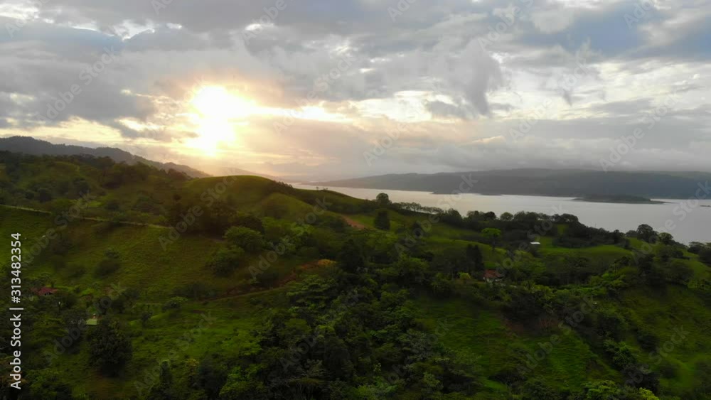 Aerial shot of approaching lake Arenal, Costa Rica. Shot over green surroundings approaching the lake at sunset. Cloudy weather. Aerial shot of approaching lake Arenal, Costa Rica. Shot over green surroundings approaching the lake at sunset. Cloudy weather.