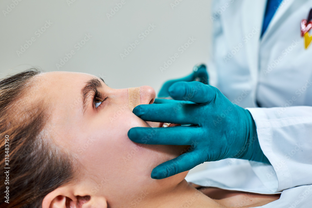 Lady with plaster on nose, doctor examining patients face after plastic surgery Lady with plaster on nose, doctor examining patients face after plastic surgery