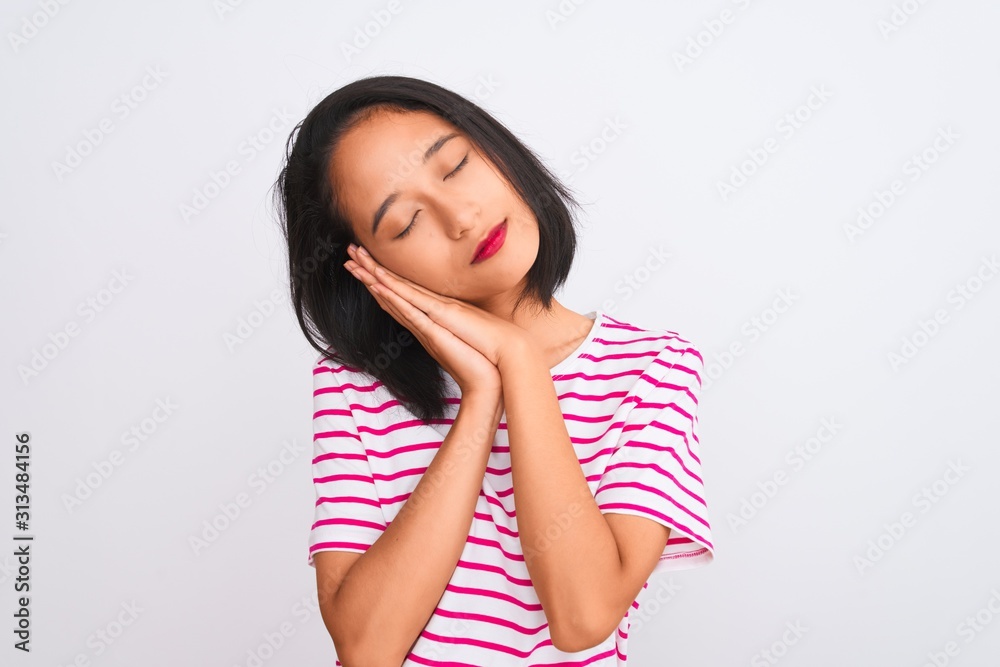 Young chinese woman wearing striped t-shirt standing over isolated white background sleeping tired dreaming and posing with hands together while smiling with closed eyes. Young chinese woman wearing striped t-shirt standing over isolated white background sleeping tired dreaming and posing with hands together while smiling with closed eyes.