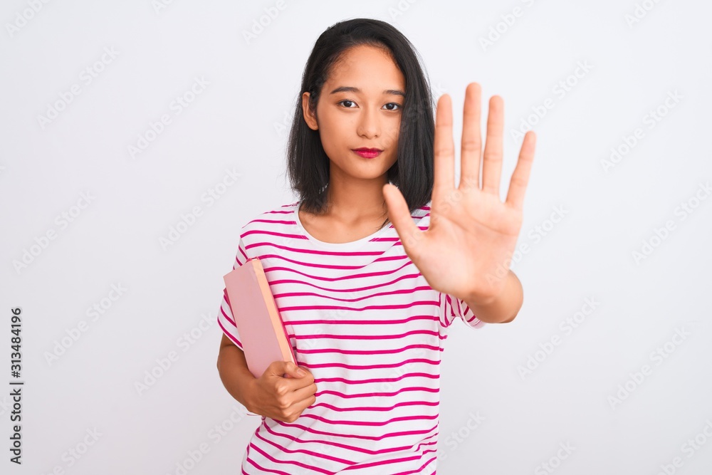 Young beautiful chinese woman holding books standing over isolated white background with open hand doing stop sign with serious and confident expression, defense gesture