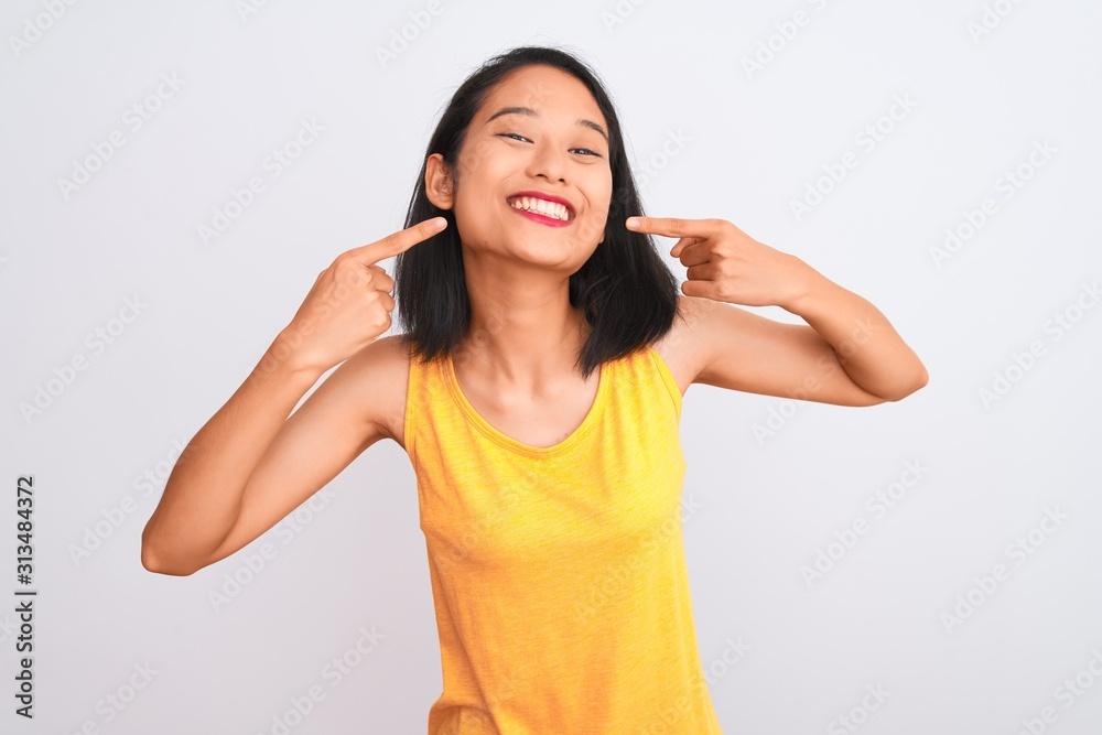 Young chinese woman wearing yellow casual t-shirt standing over isolated white background smiling cheerful showing and pointing with fingers teeth and mouth. Dental health concept. Young chinese woman wearing yellow casual t-shirt standing over isolated white background smiling cheerful showing and pointing with fingers teeth and mouth. Dental health concept.