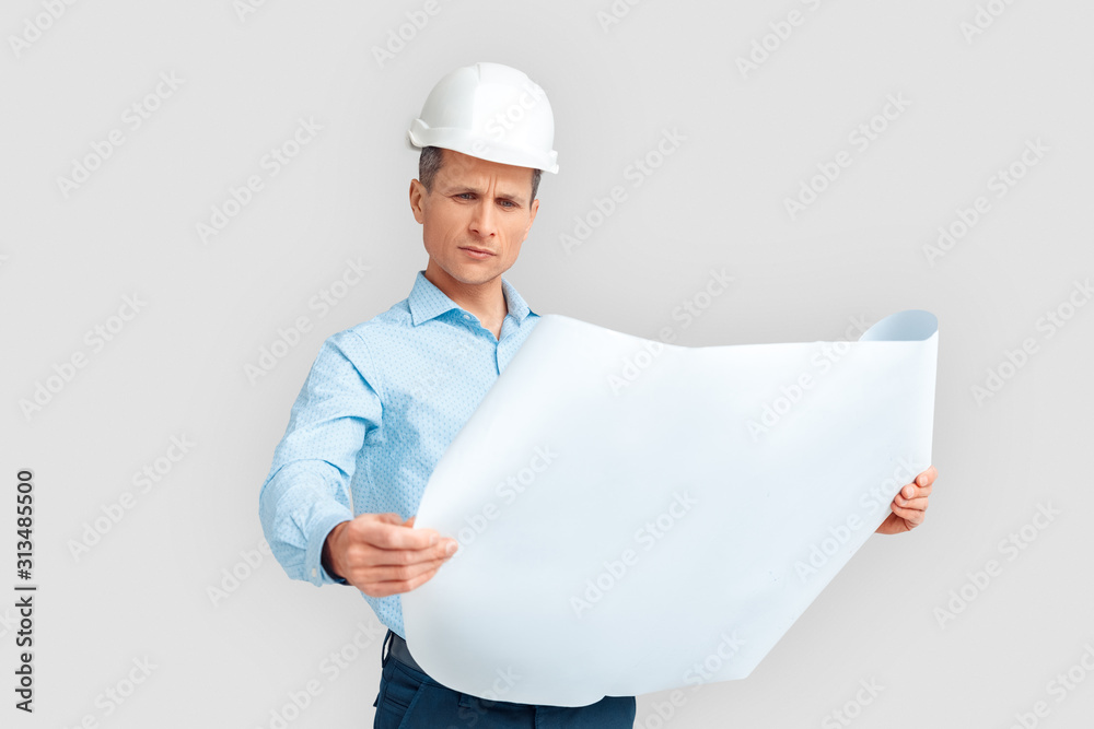 Construction. Mature man in hardhat standing isolated on white with blueprint studying concerned Construction. Mature man in hardhat standing isolated on white with blueprint studying concerned