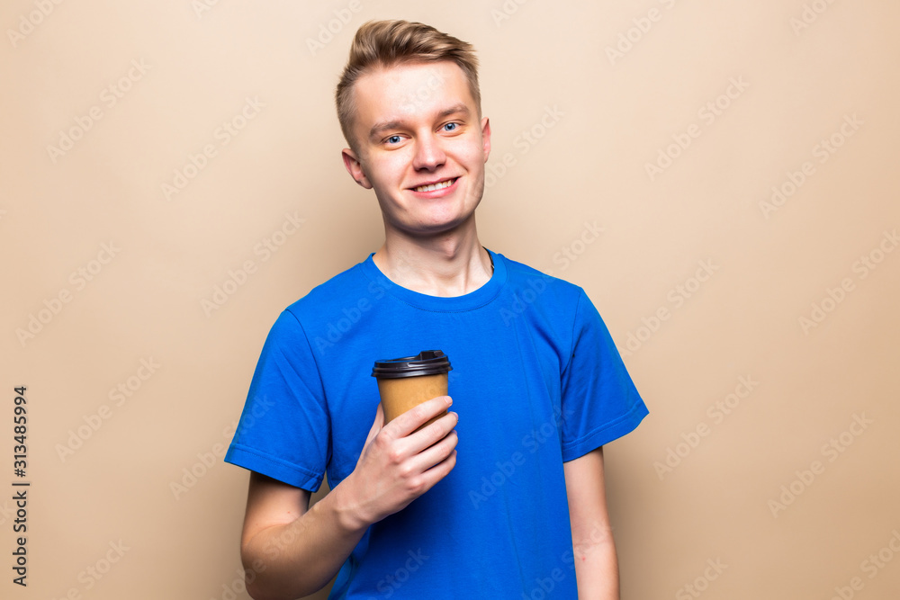 Young man smiling while holding coffee cup isolated over beige background Young man smiling while holding coffee cup isolated over beige background