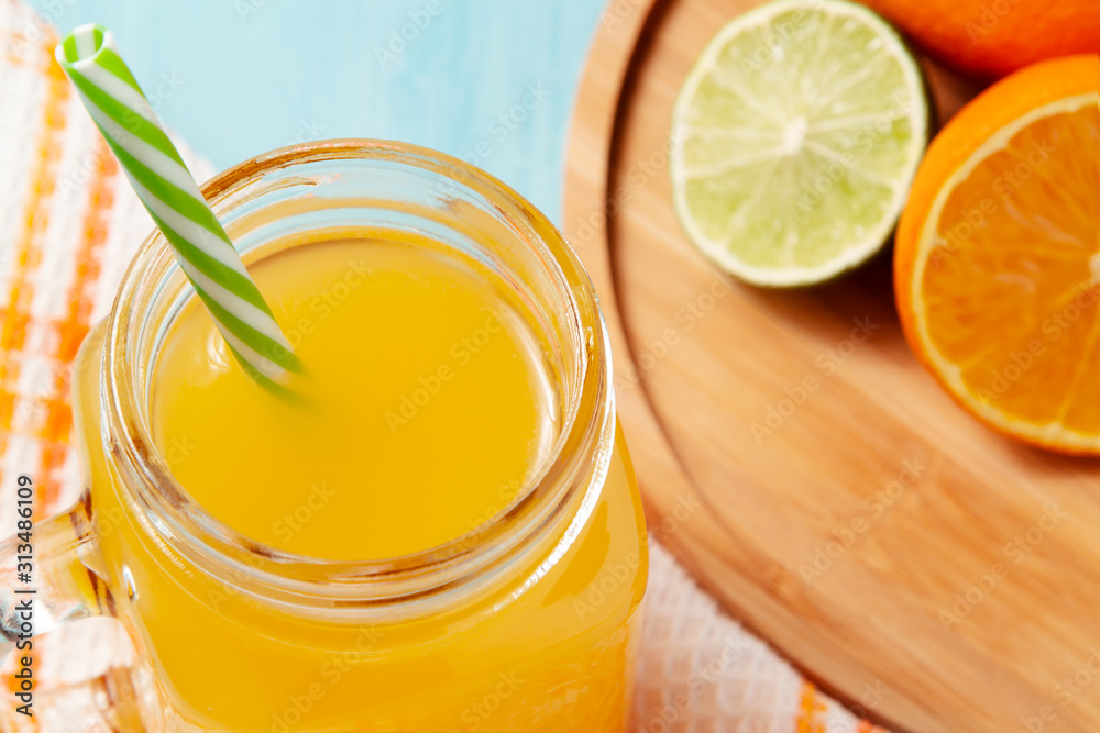 Homemade freshly squeezed orange juice in a mason jar, oranges and lime on wooden dish closeup Homemade freshly squeezed orange juice in a mason jar, oranges and lime on wooden dish closeup