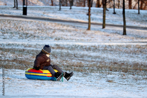 Child having fun on snow tube in a park, boy sliding down the hill. Winter entertainment, sledding in frosty day