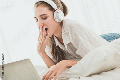 Beautiful woman yawning front of laptop computer while laying on bed
