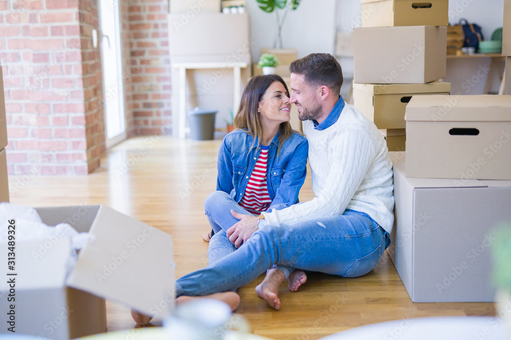 Young beautiful couple sitting on the floor at new home around cardboard boxes Young beautiful couple sitting on the floor at new home around cardboard boxes