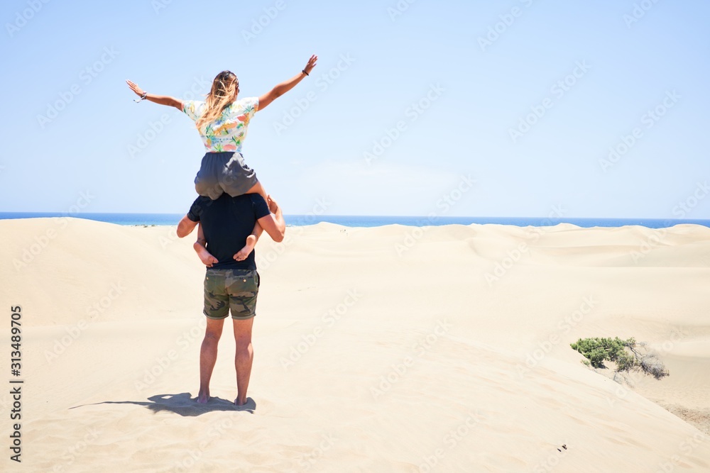 Plakat Young beautiful couple smiling happy and confident. Woman sitting on man shoulders with smile on face at the beach