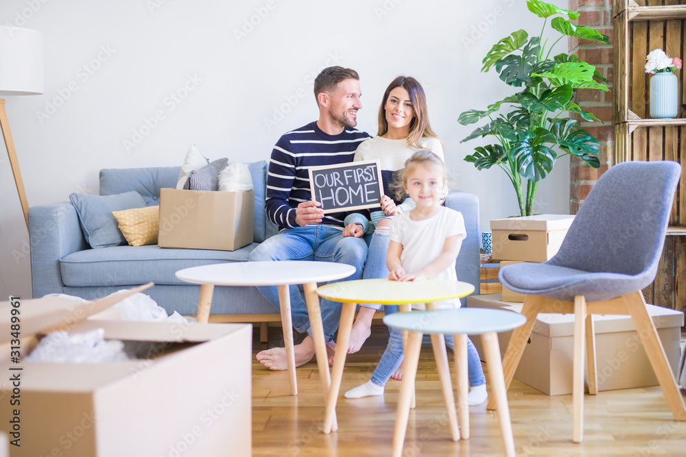 Beautiful famiily with kid sitting on the sofa holding blackboard at new home around cardboard boxes Beautiful famiily with kid sitting on the sofa holding blackboard at new home around cardboard boxes