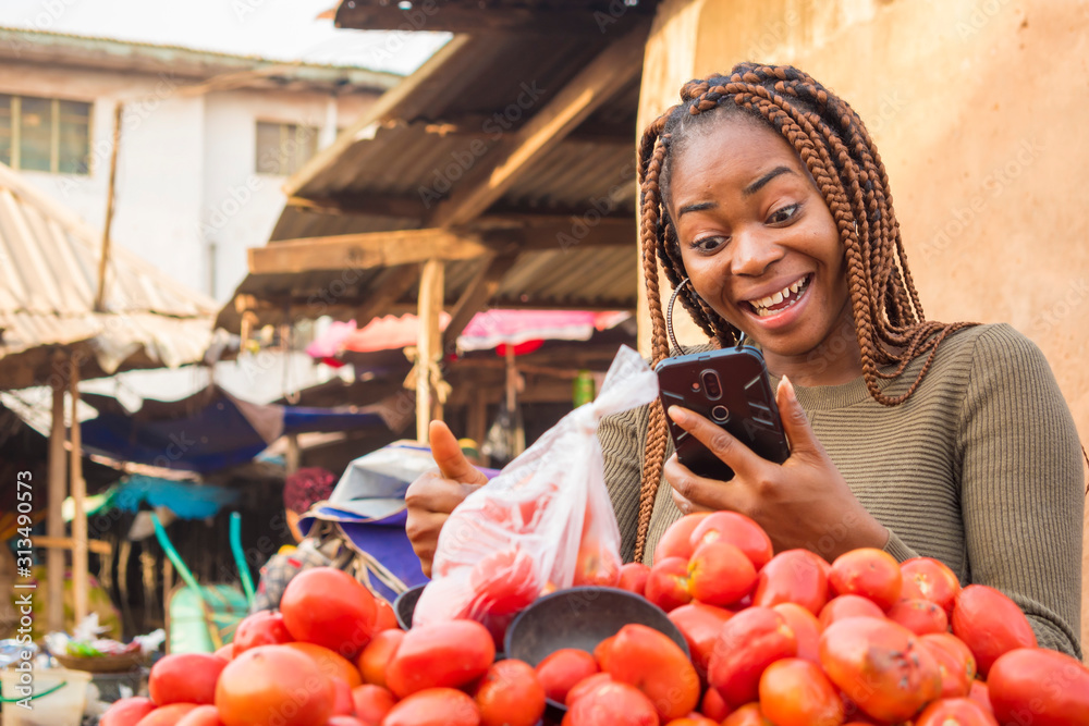 beautiful young african woman in a local african market viewing content on her phone feeling surprised