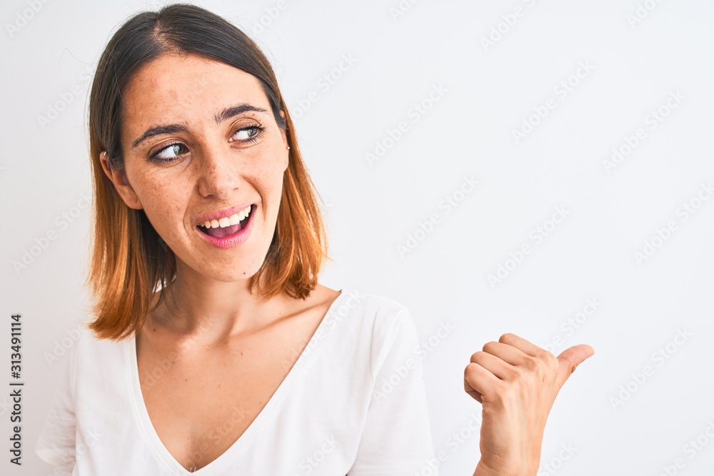 Beautiful redhead woman wearing casual white t-shirt over isolated background pointing and showing with thumb up to the side with happy face smiling Beautiful redhead woman wearing casual white t-shirt over isolated background pointing and showing with thumb up to the side with happy face smiling