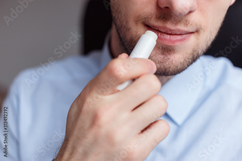 Man applying hygienic lipstick on lips to revive chapped lips and avoid dry, closeup photo