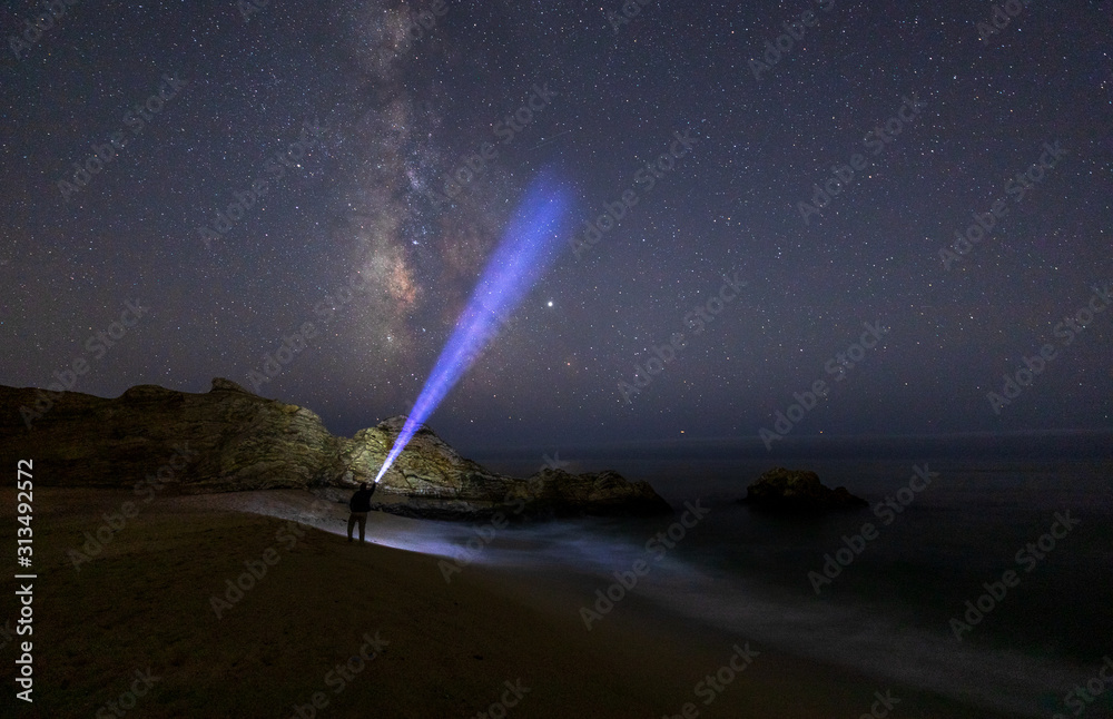 The Milky Way off the coast of Half Moon Bay, Northern California with a man holding a flashlight pointing up into the sky