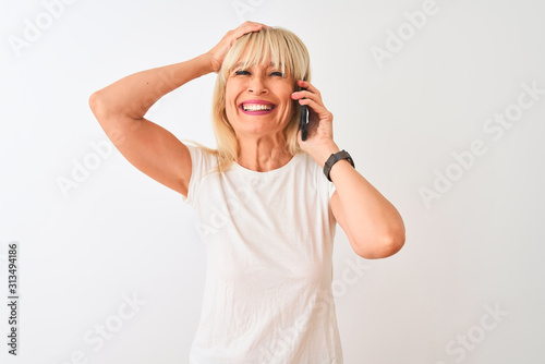 Middle age woman talking on the smartphone standing over isolated white background stressed with hand on head, shocked with shame and surprise face, angry and frustrated. Fear and upset for mistake.